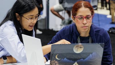 A conference attendee works with an Esri expert at a laptop