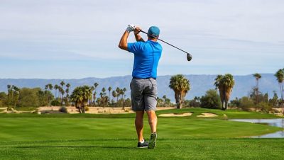 Player completing a swing on a golf course with palm trees and distant mountains