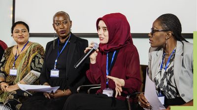 Four people sitting side-by side with one speaking into a microphone