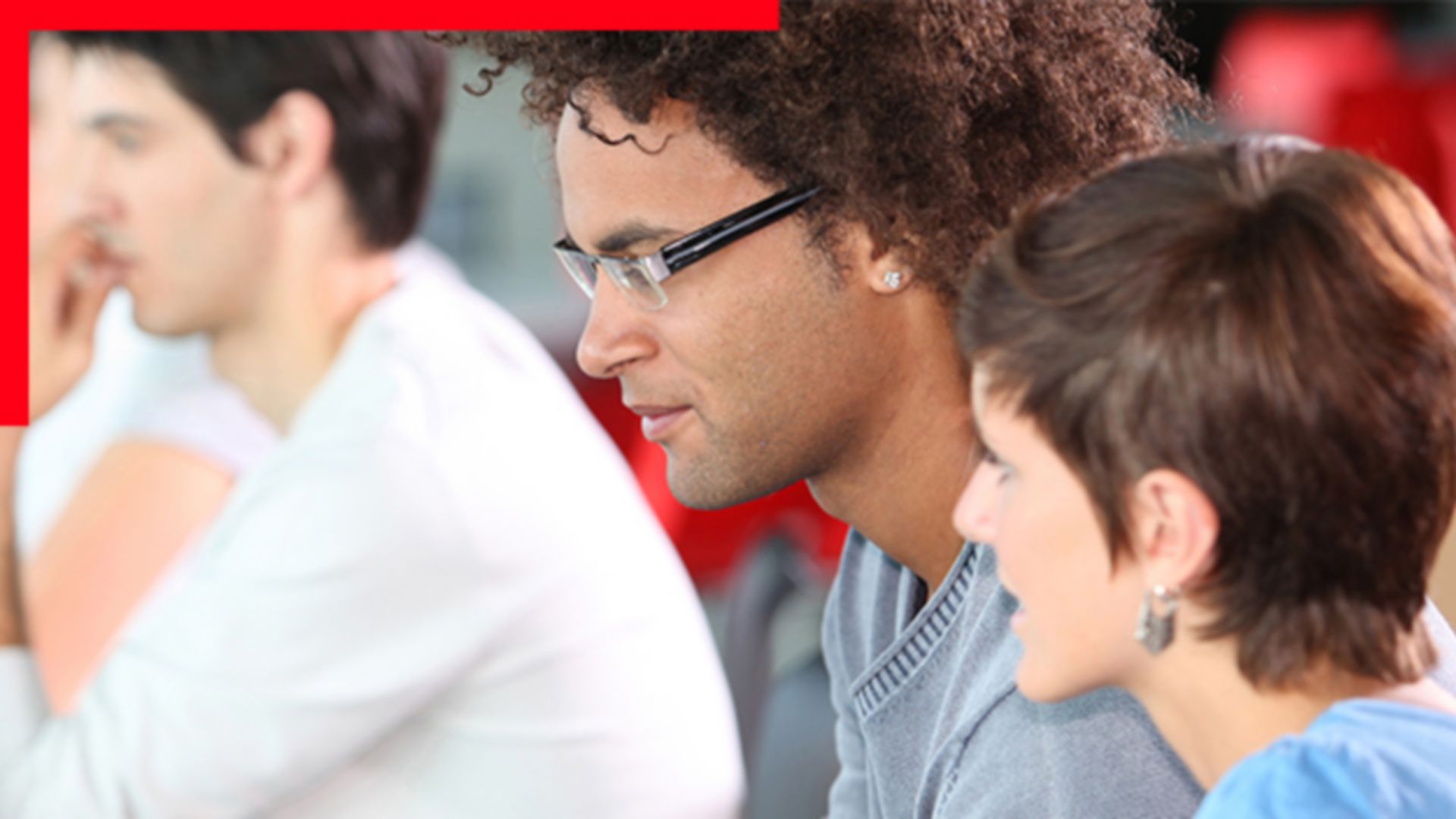 Photo of three casually dressed attendees in a group seminar setting gazing to the left at an unseen speaker or screen