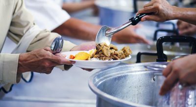 A close-up image of hands serving a plate of food at a community kitchen. 