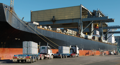 Trucks transporting cargo to a large shipping boat that is docked and loading