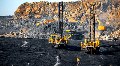 Drilling machines, bulldozers, and dump trucks work in a charred mine field 
