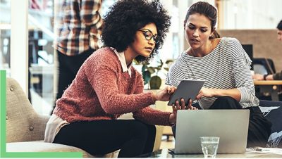 Two people sitting in a coffee shop working with GIS software on a tablet and laptop