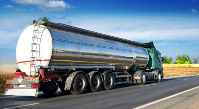 A green and silver big rig driving down a highway beside a large stretch of brown farmland beneath a deep blue sky streaked with clouds
