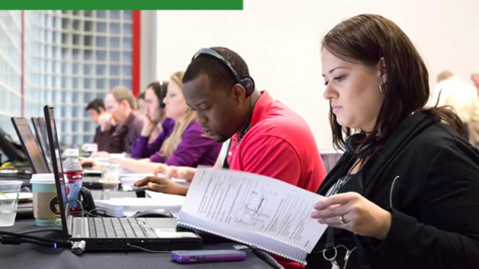 A group of people sitting at a long desk with laptop computers taking individual training courses