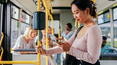 Standing bus passenger checks route information on a cell phone