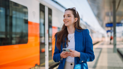 Passenger on a train platform hlds a cek hone and looks to the left