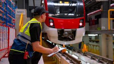 A person wearing a safety vest performing an inspection on a rail car in a train station