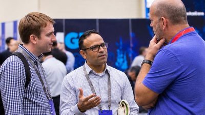 Three men stand together engaged in conversation at an indoor event or conference