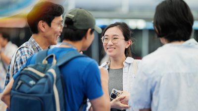 A group of four people stand together in conversation with one person holding a phone