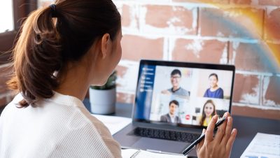 Person seated at a desk participating in a video call on a laptop and gesturing toward the screen