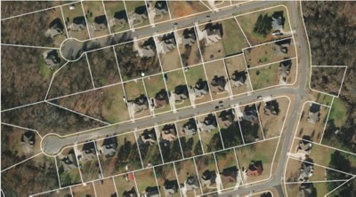 This is a screenshot of a desktop application. The application is used to view and edit geospatial data. The image shows a map of a city. The map is made up of several layers, including a layer of aerial imagery, a layer of tax parcels, and a layer of streets. The user is currently editing the layer of tax parcels. The user has selected a parcel and is viewing its attributes.