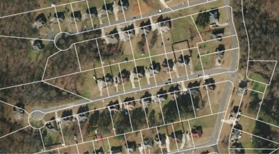 This is a screenshot of a desktop application. The application is used to view and edit geospatial data. The image shows a map of a city. The map is made up of several layers, including a layer of aerial imagery, a layer of tax parcels, and a layer of streets. The user is currently editing the layer of tax parcels. The user has selected a parcel and is viewing its attributes.