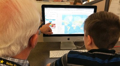 Educator pointing to computer screen with map next to student.