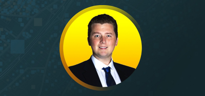 黄色と青緑色の背景にビジネス スーツを着て微笑む Kyle Duncan