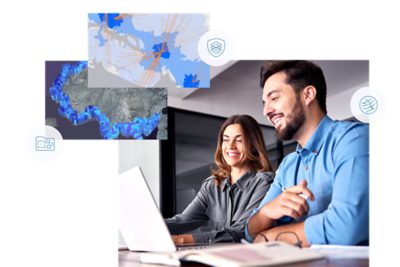 Two women smiling while collaborating on a computer. Above them are two illustrations of city maps in blue and white.