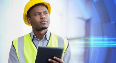 A worker wearing a hard hat and safety vest holds a mobile device.