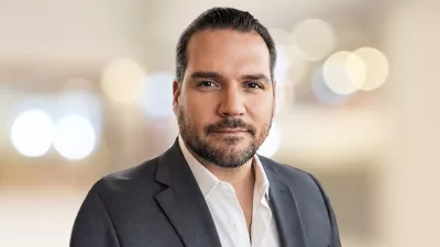 Joe sorrindo de terno diante de um fundo neutro em foco suave