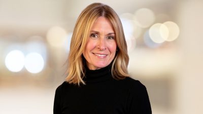 Stacy sorrindo com uma gola alta preta diante de um fundo neutro em foco suave