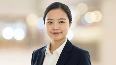 Suki sorrindo de camisa e blazer diante de um fundo neutro em foco suave