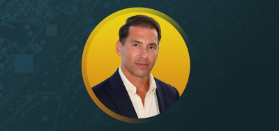 Nick DiPaolo smiling in front of a yellow and teal background