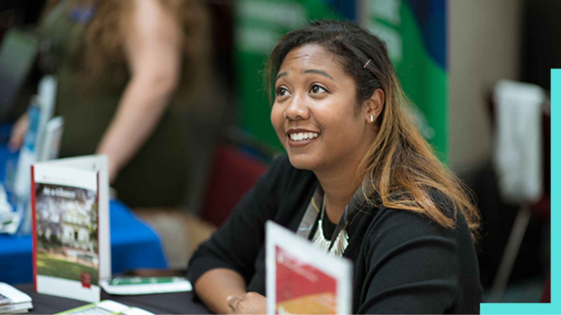 A woman is seated at a booth during an indoor event or conference.