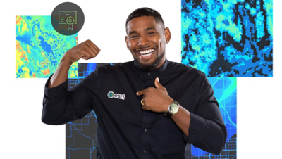 A smiling man in a black shirt points to the Esri logo on the chest and he is against a background of maps