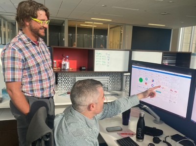 Two men by a desk in an office talking and looking at a computer monitor