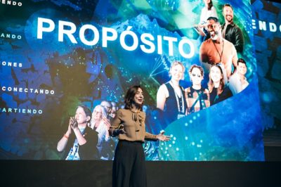 Jack Dangermond smiling and wearing a blue suit against a background of colorful abstract graphics