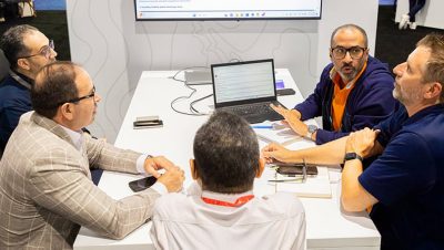 A group of people gathered around a table in an office looking at a laptop and discussing content on the screen