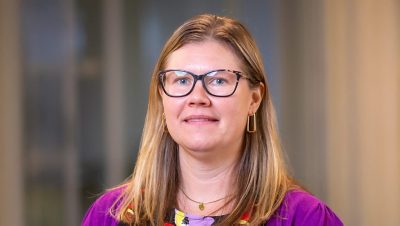 Portrait of Renee Opatz in a bright patterned shirt and sweater with a blurred office background