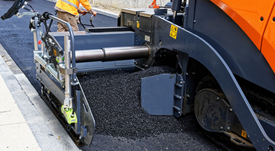 A close-up view of a road paving machine distributing fresh asphalt onto a street.