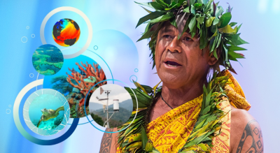 A man in mid-speech wearing a traditional yellow shawl and leaf leis around his head and neck, overlaid with small images of a globe, a coral reef, a sea turtle, and a weather station