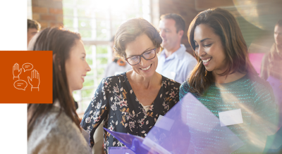 Three women in a group smiling and looking at a binder