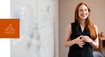A smiling young woman in front of a white board holding a marker