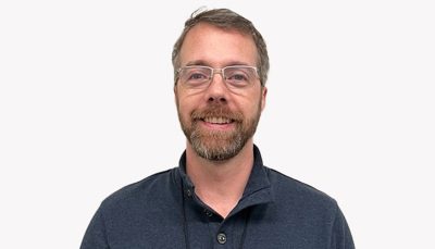 Kyle Martinez smiling in glasses and a gray shirt in front of a white background 