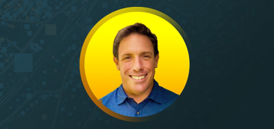 黄色と青緑色の背景に青いワイシャツを着て微笑んでいる Steven Hochart