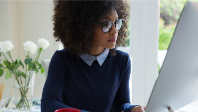 A woman working on her desktop computer and looking at a large monitor