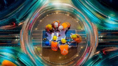 Vista cenital de ingenieros revisando planos sobre una autopista nocturna con luces en movimiento.