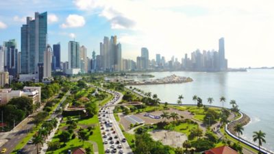 Paisaje urbano de la costa de Panamá con edificios modernos, un parque y una avenida con tráfico.