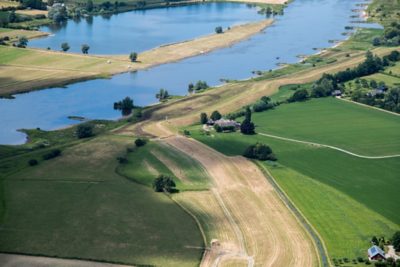 Landschap met rustig water, groen veld en een aantal huizen