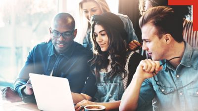 A group of young adults gathers closely around a laptop, engaged in a collaborative activity. 