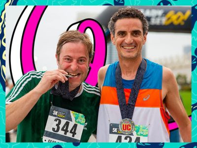 Two runners wearing race bibs and medals posing together at the finish line of the 5K