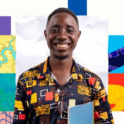 A person wearing a colorful geometric-patterned shirt holding a notebook and smiling broadly.