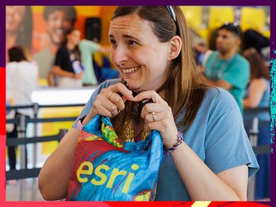 Smiling woman with brown hair holds a colorful blue, red, and yellow bag labeled Esri in yellow text