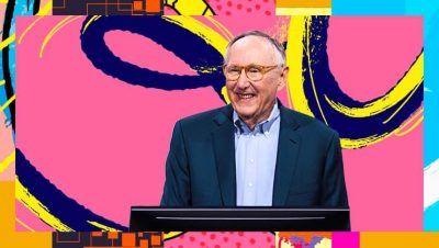 Jack Dangermond smiling and wearing a blue suit against a background of colorful abstract graphics
