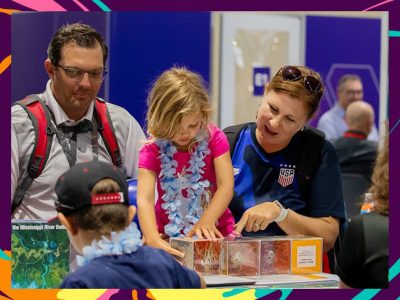 Child engaging in a hands-on activity at a table with adults nearby and educational materials and colorful decorations visible
