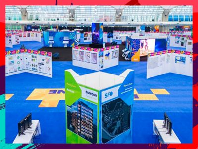 A large brightly lit exhibition hall filled with assorted colorful display booths showcasing maps and informational panels