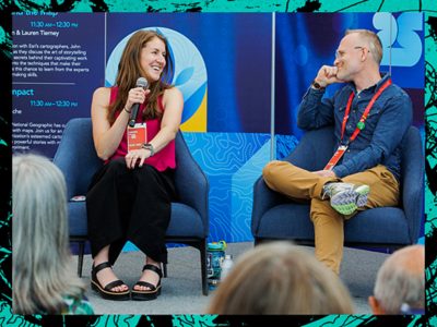 Two smiling Esri experts seated in blue armchairs leading a presentation as one holds a micrphone